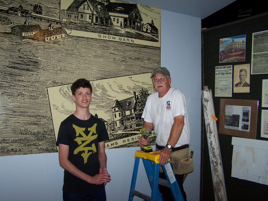 Volunteers, Joseph Neumann and Gary White (on the ladder) work on hanging the newest display at Hartland Acres.